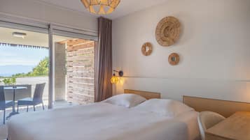 Habitación de hotel con una cama grande, un balcón con sillas y vistas al exterior.