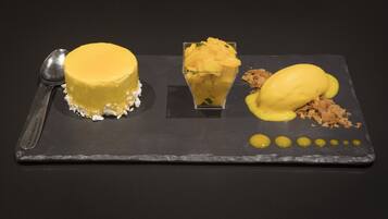 A dessert plate with a yellow cake, a glass of mango puree, and a scoop of ice cream on a slate serving board.
