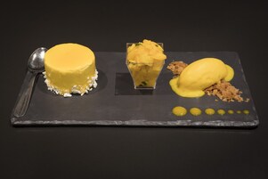 A dessert plate with a yellow cake, a glass of mango puree, and a scoop of ice cream on a slate serving board.