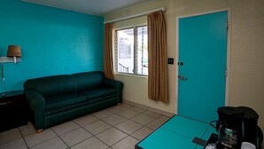 Une pièce aux murs de couleur turquoise, avec un canapé vert, une machine à café posée sur une table et une porte dotée d’une fenêtre.