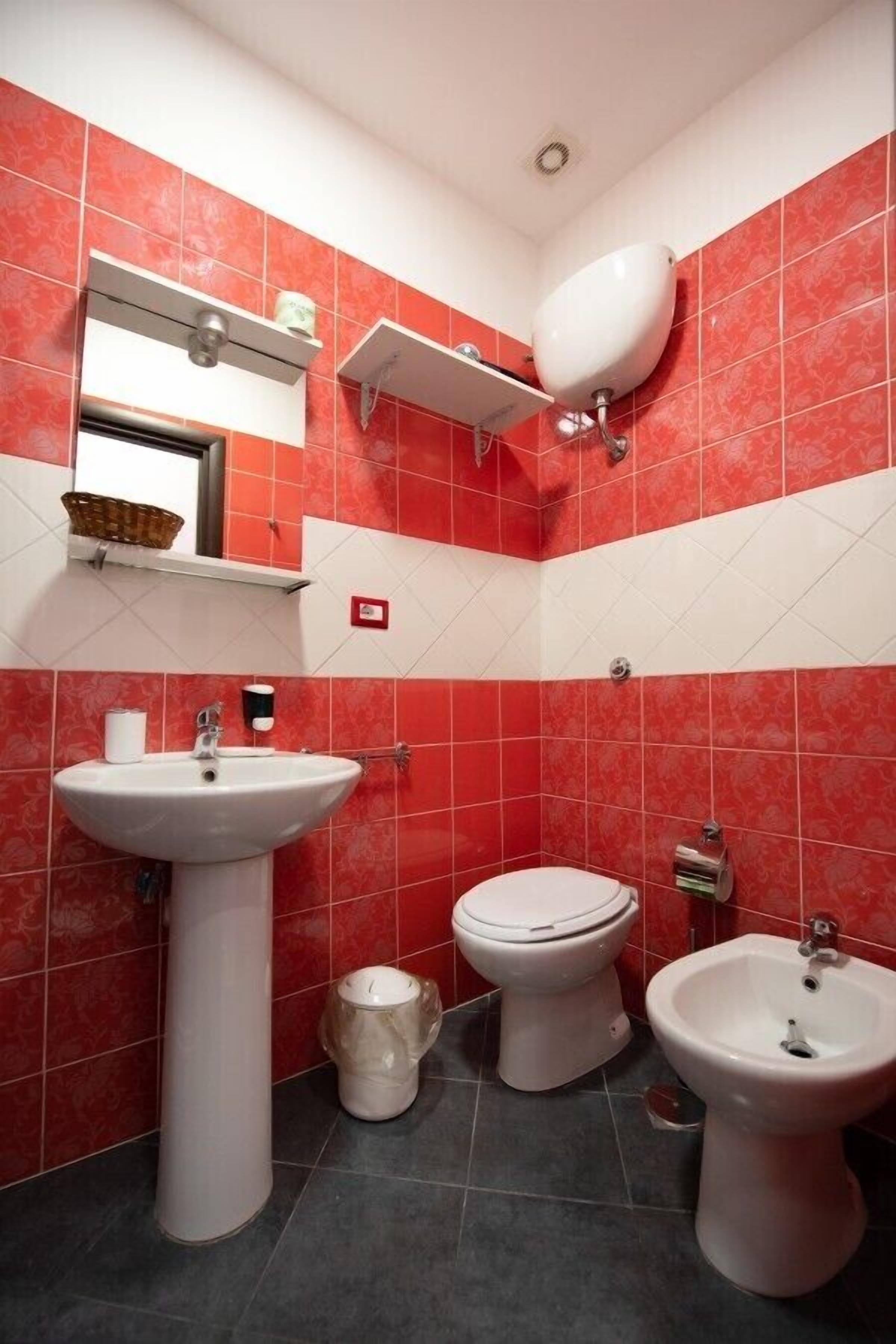 A bathroom with red and white tiles, a white sink, a toilet, and a bidet.