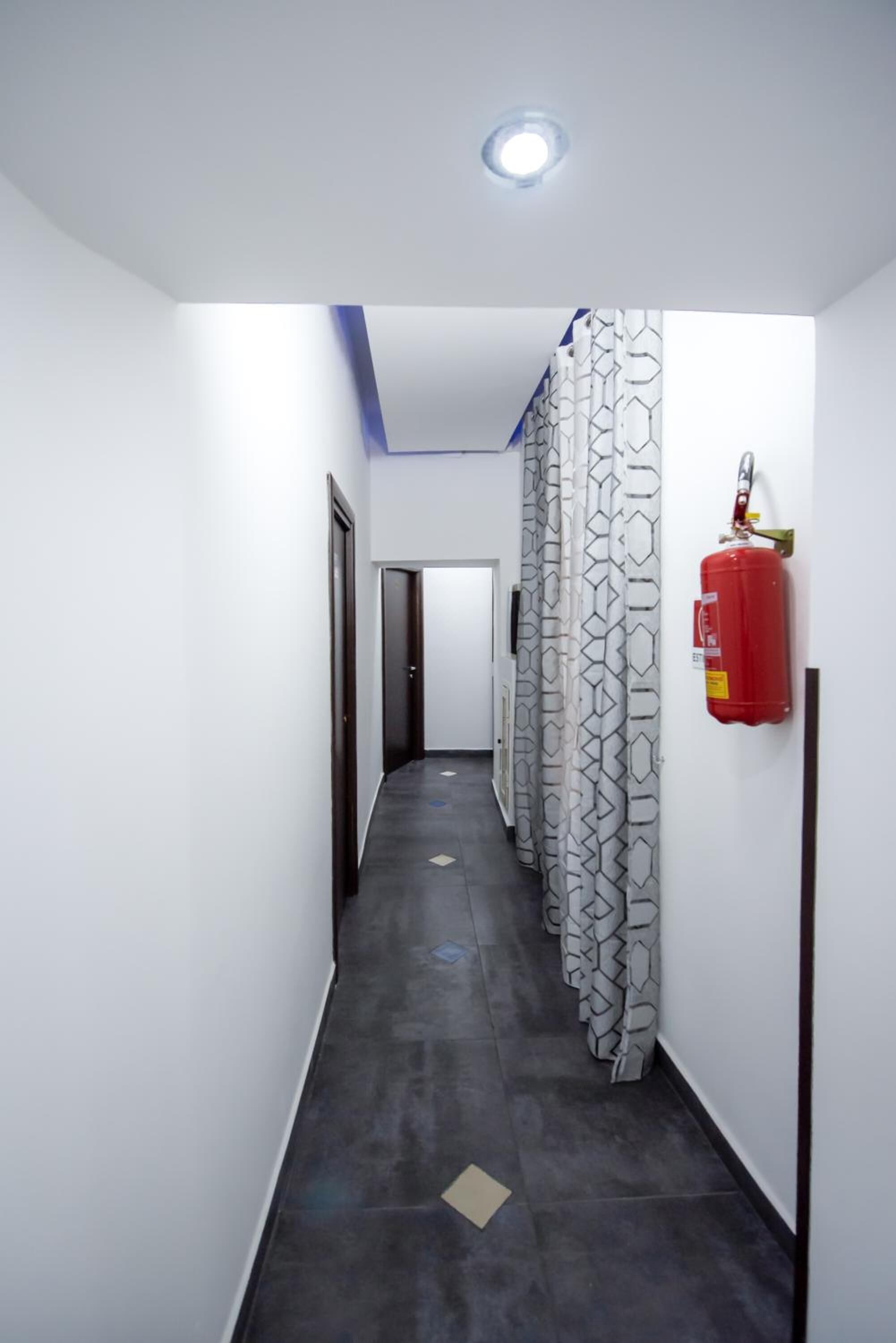 A narrow hallway with a patterned curtain, a fire extinguisher, and a door at the end.