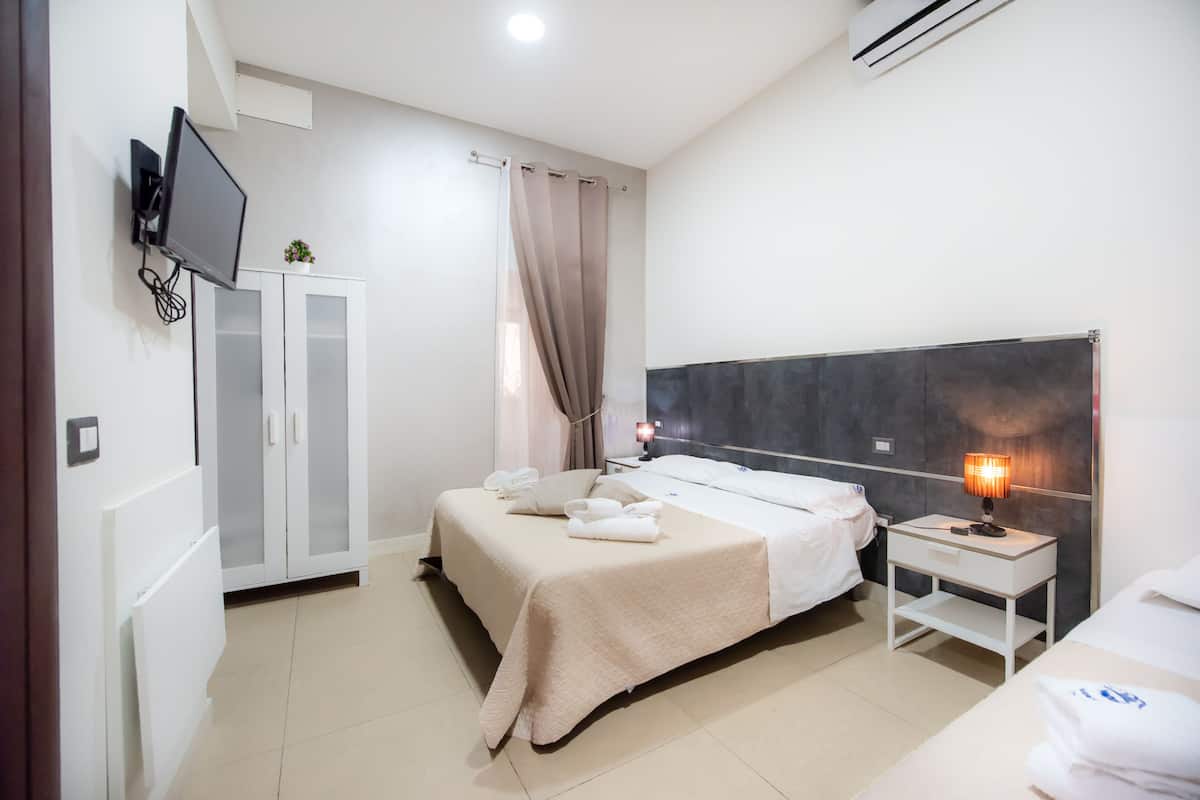 A hotel room with a bed, bedside table, TV, wardrobe, and a small plant.