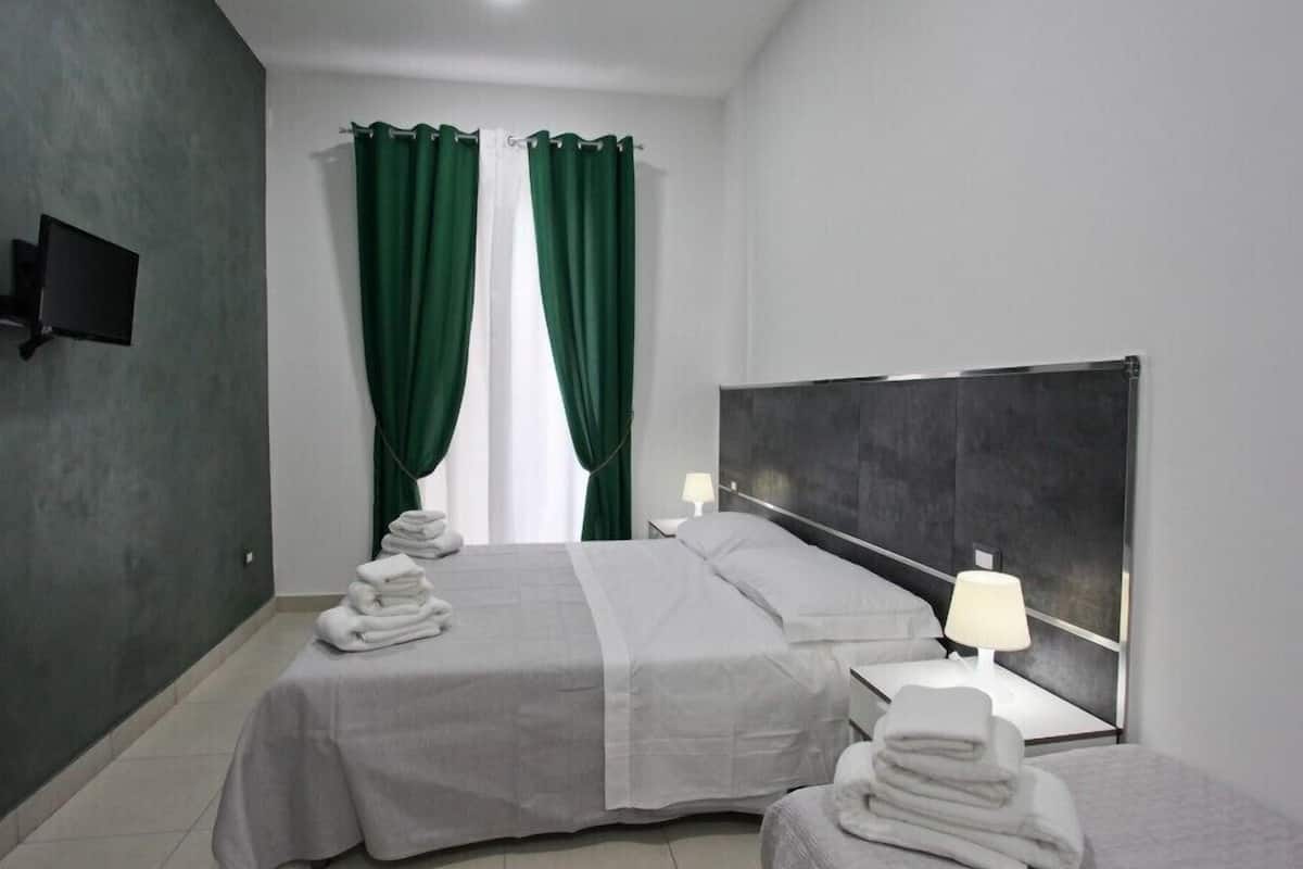 A modern hotel room with two beds, a flat-screen TV on the wall, and a window with green curtains.