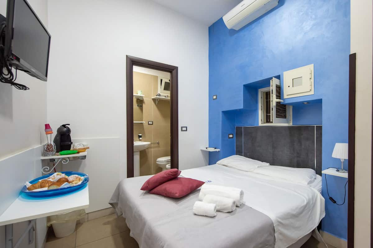 A hotel room with a bed, a TV, a desk with a tray of pastries, a sink, and a mirror.