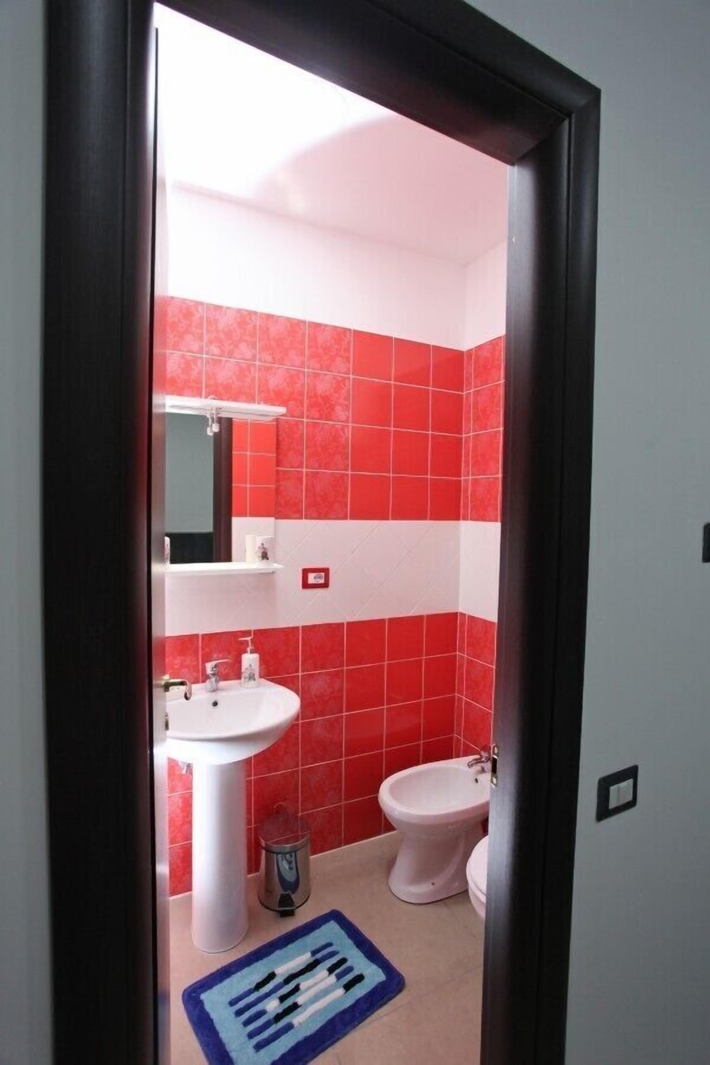 Un bagno con piastrelle rosse e bianche, un lavandino bianco, un bidet e un tappeto blu e bianco.