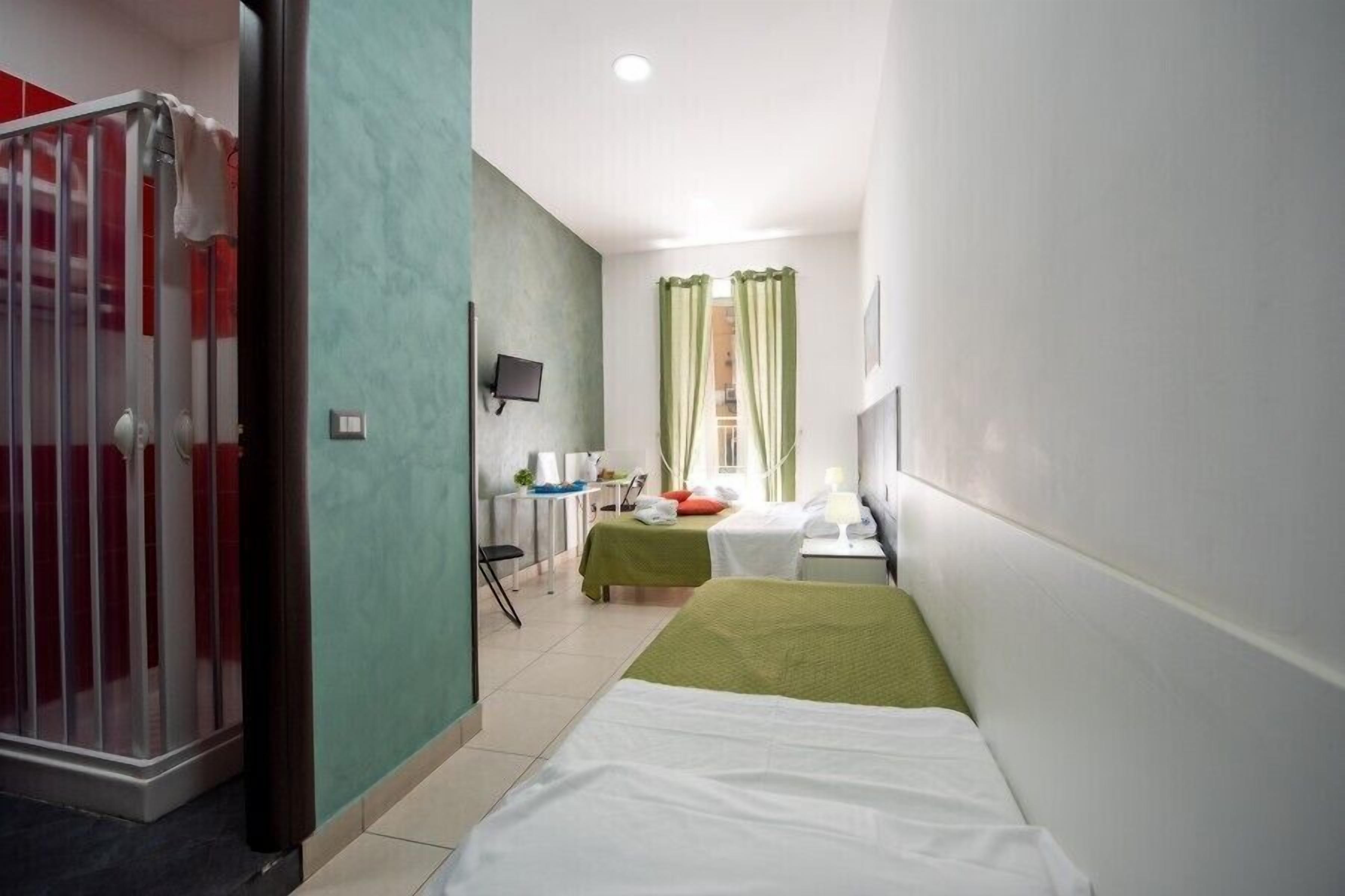 A hotel room with two beds, a desk with a chair, a TV, and a window with curtains.