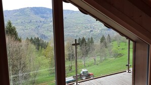 A room with large windows offering a view of a green landscape with hills and a tractor on a wooden deck.