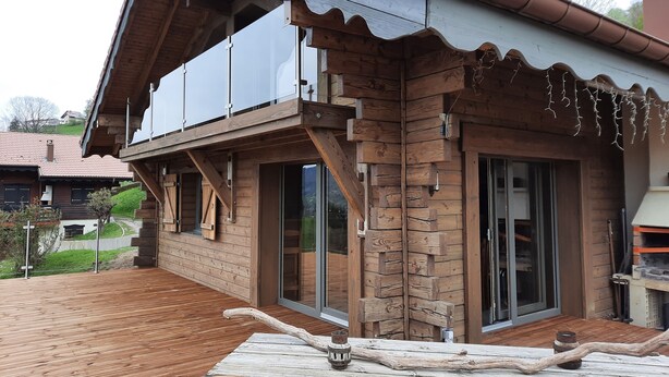 A wooden cabin with a balcony, large windows, and a wooden deck.