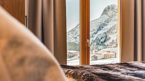 Une chambre à coucher avec vue sur un paysage montagneux enneigé, visible à travers une fenêtre ornée de rideaux.