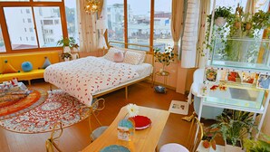 Une chambre confortable avec un lit, une table à manger, des chaises, un canapé et une fenêtre donnant sur des immeubles.