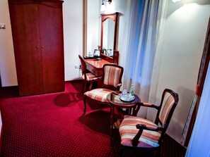 A hotel room with a wooden wardrobe, a dining table with chairs, a small round table with a bottle and glasses, and a mirror on the wall. - Hotel Villa Royal (Ostrow Wielkopolski)