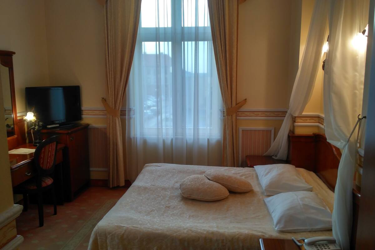A hotel room with a bed, a desk with a television, a chair, and a telephone.
