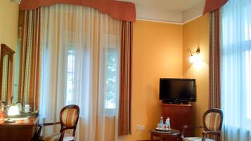 A hotel room with a television, two chairs, a small table with water bottles, and a lamp.