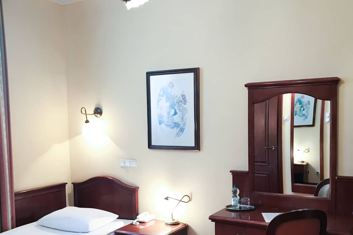 A hotel room with a bed, bedside table, desk, chair, and a mirror.