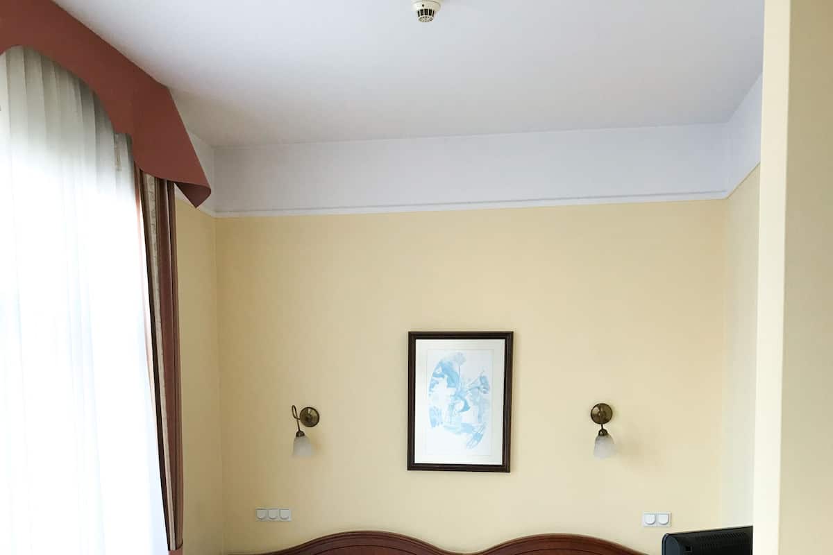 A hotel room with a bed, a bedside table with a lamp, a framed picture on the wall, and a television.