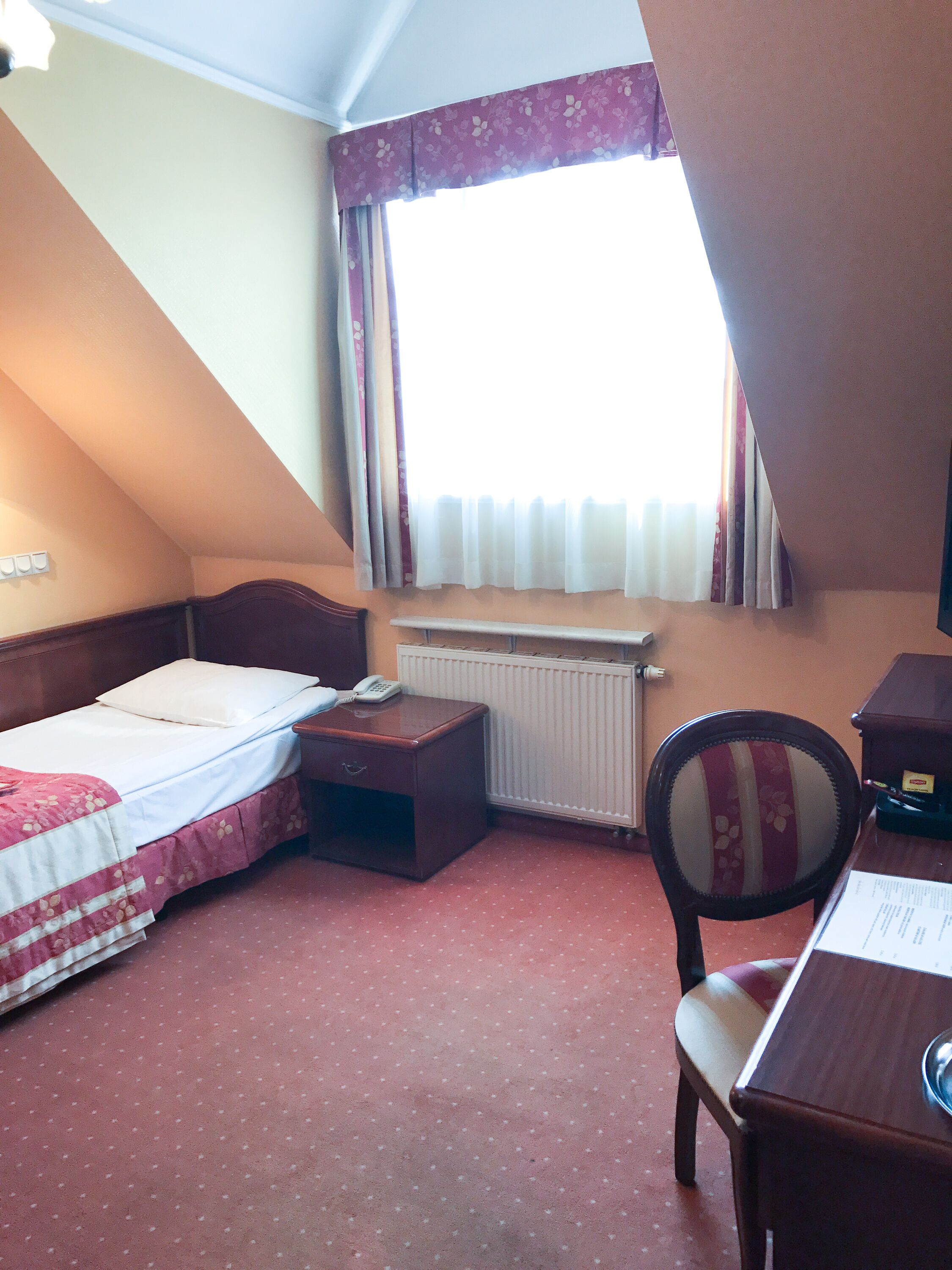 A small, cozy hotel room with a single bed, a desk, a chair, and a radiator.