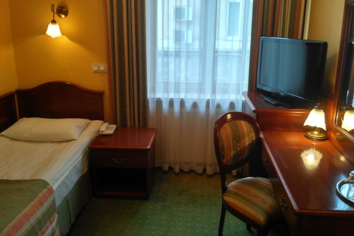 A hotel room with a bed, a desk with a television, a chair, and a nightstand.
