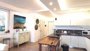 A modern kitchen with white cabinets, a wooden dining table, and a large abstract painting on the wall.