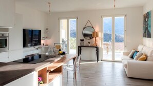 A modern kitchen with a large island, a dining area with a table and chairs, a sofa, and a large window with a view of the mountains.