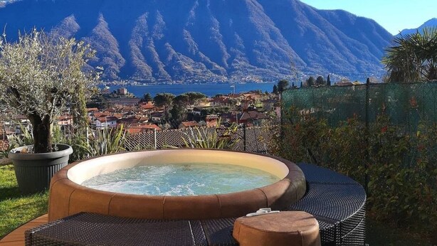 A hot tub with a mountain view, surrounded by greenery and a fence.