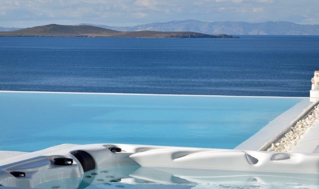 A clear view of a private infinity pool with a hot tub, overlooking a calm sea and distant mountains.
