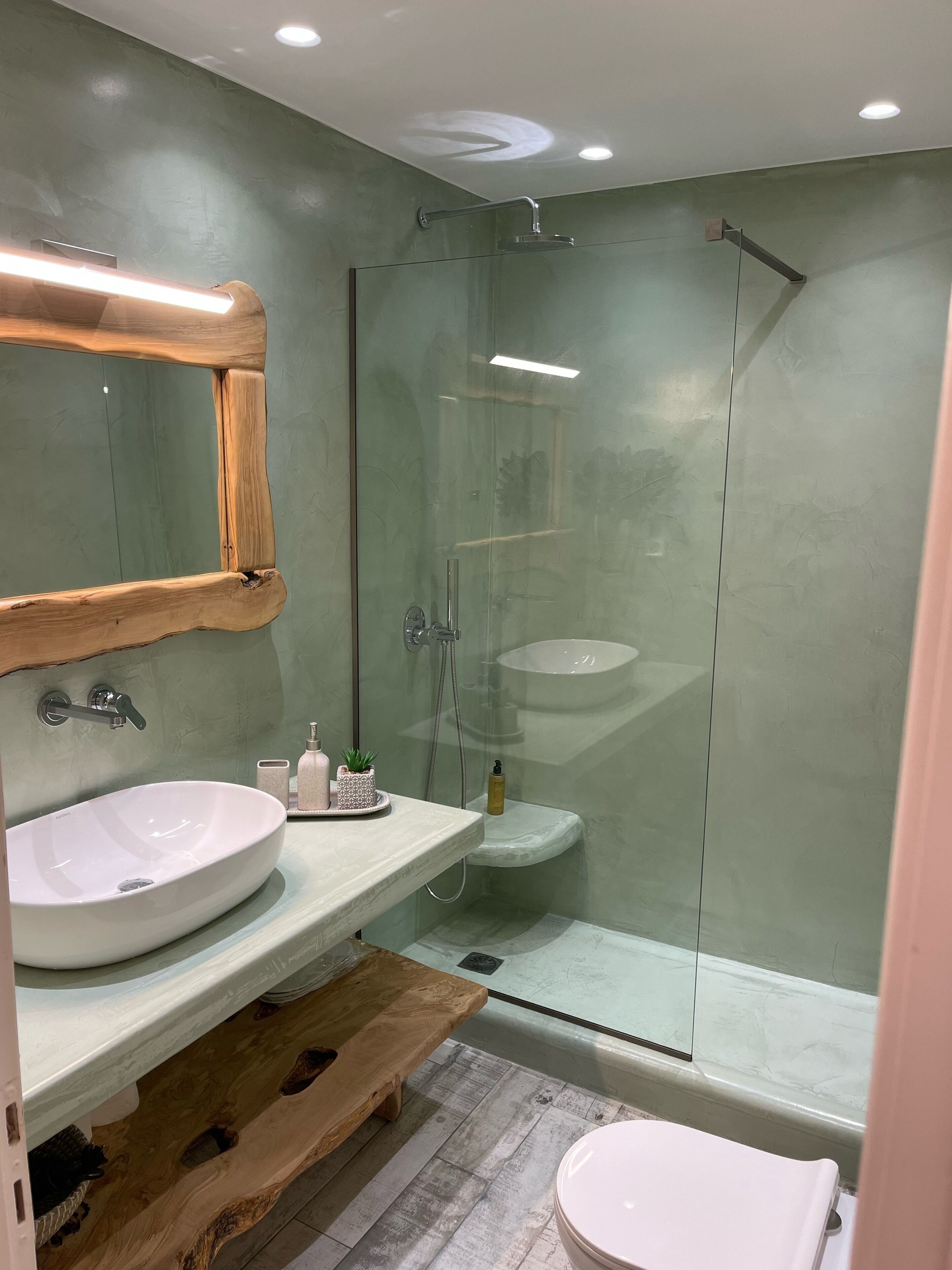 Een moderne badkamer met een houten wastafelmeubel, een grote spiegel, een douchecabine van glas en een marmeren wastafel.