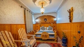 A wooden-paneled room with a bed, a wooden chair, and a patterned rug. - Mount Toubkal Lodge (Asni)