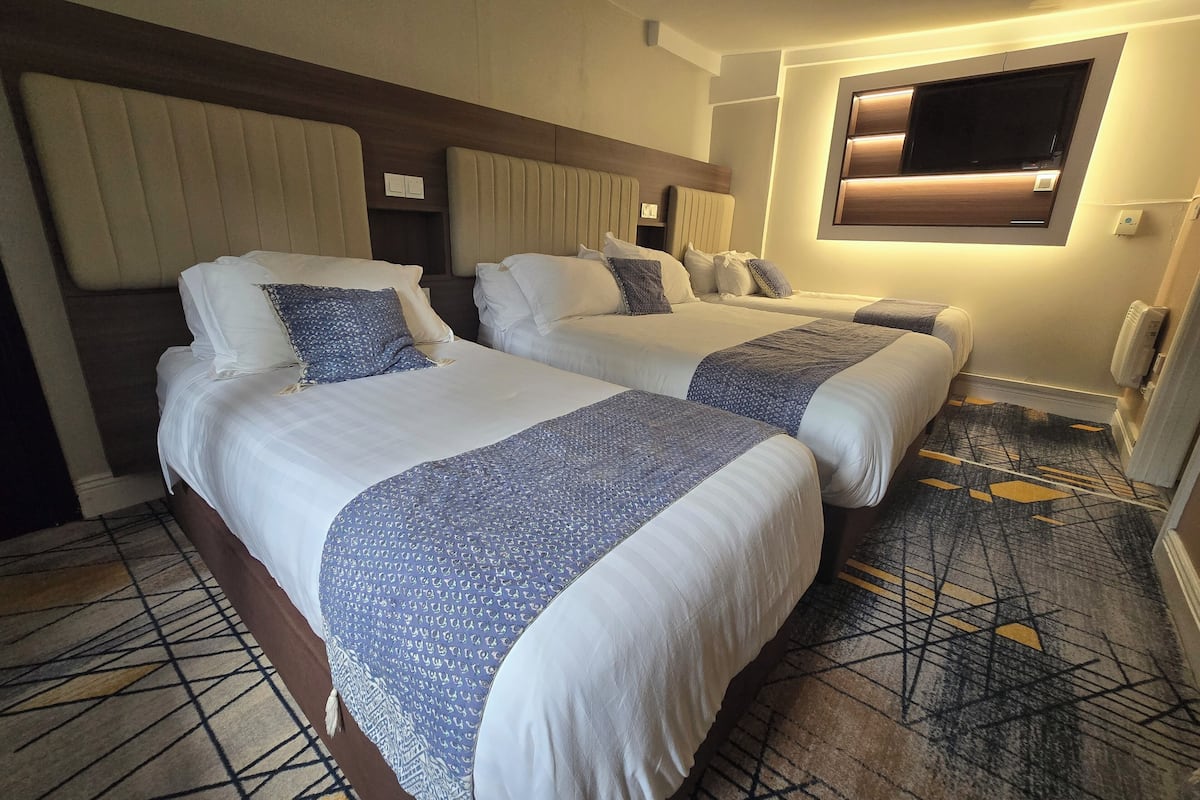 A hotel room with two beds, a TV mounted on the wall, and a patterned carpet.