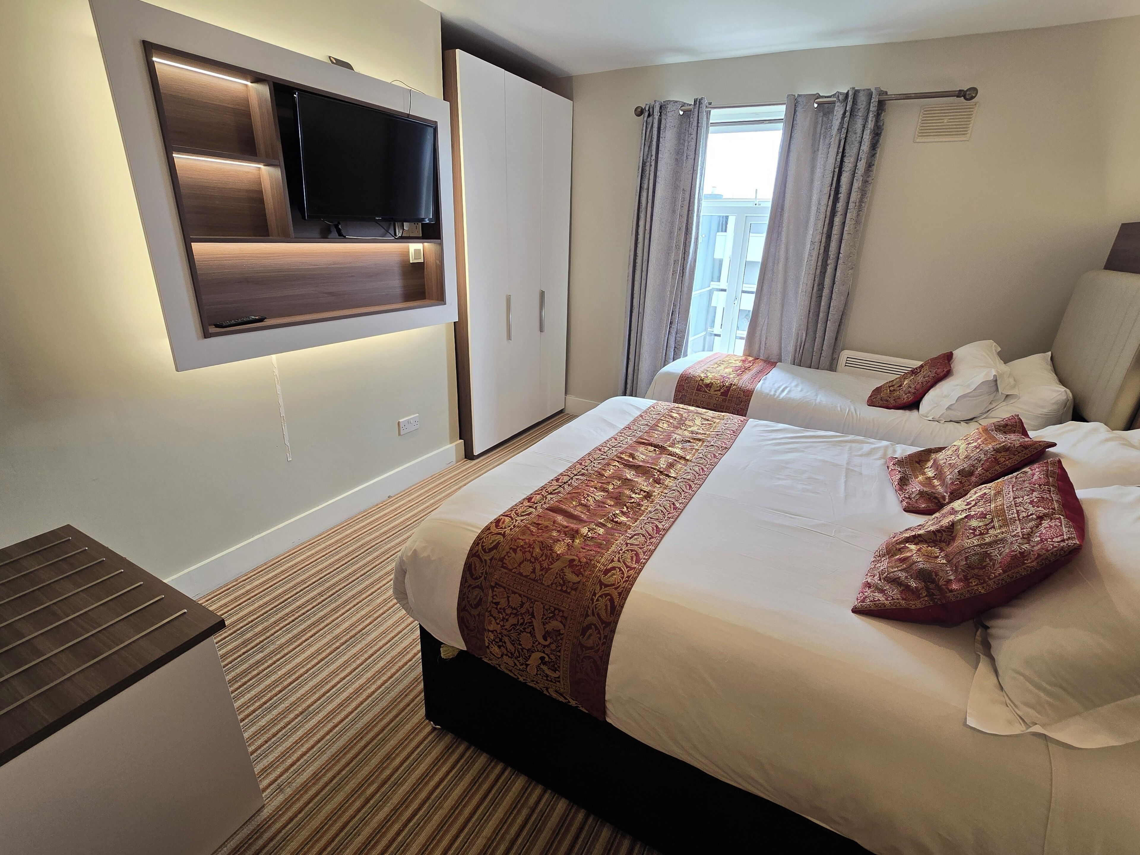 Une chambre d’hôtel avec un grand lit, un téléviseur fixé au mur et une fenêtre avec des rideaux.
