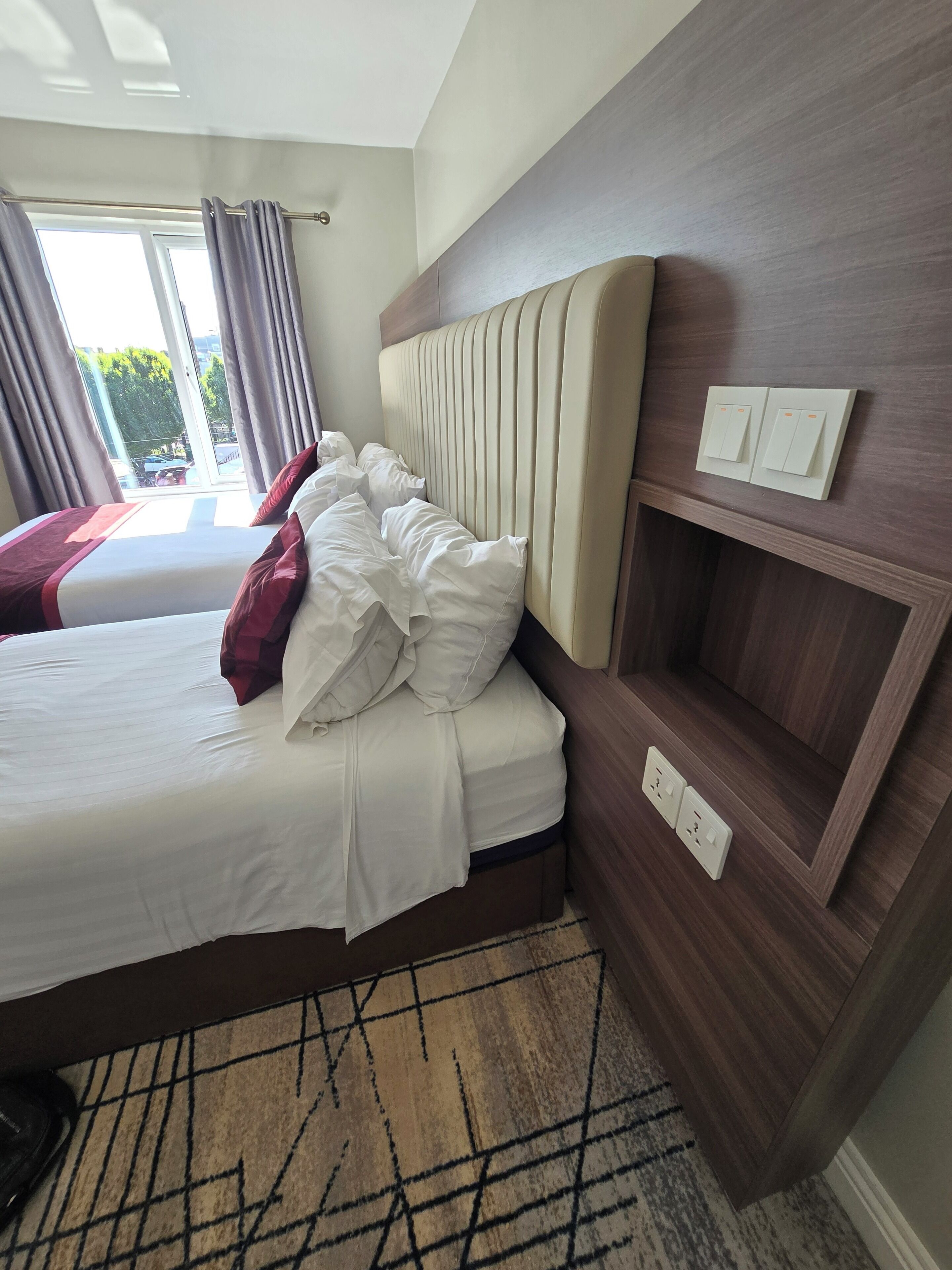 Habitación de hotel con una cama grande, cabecera con estante incorporado y vistas al exterior por la ventana.