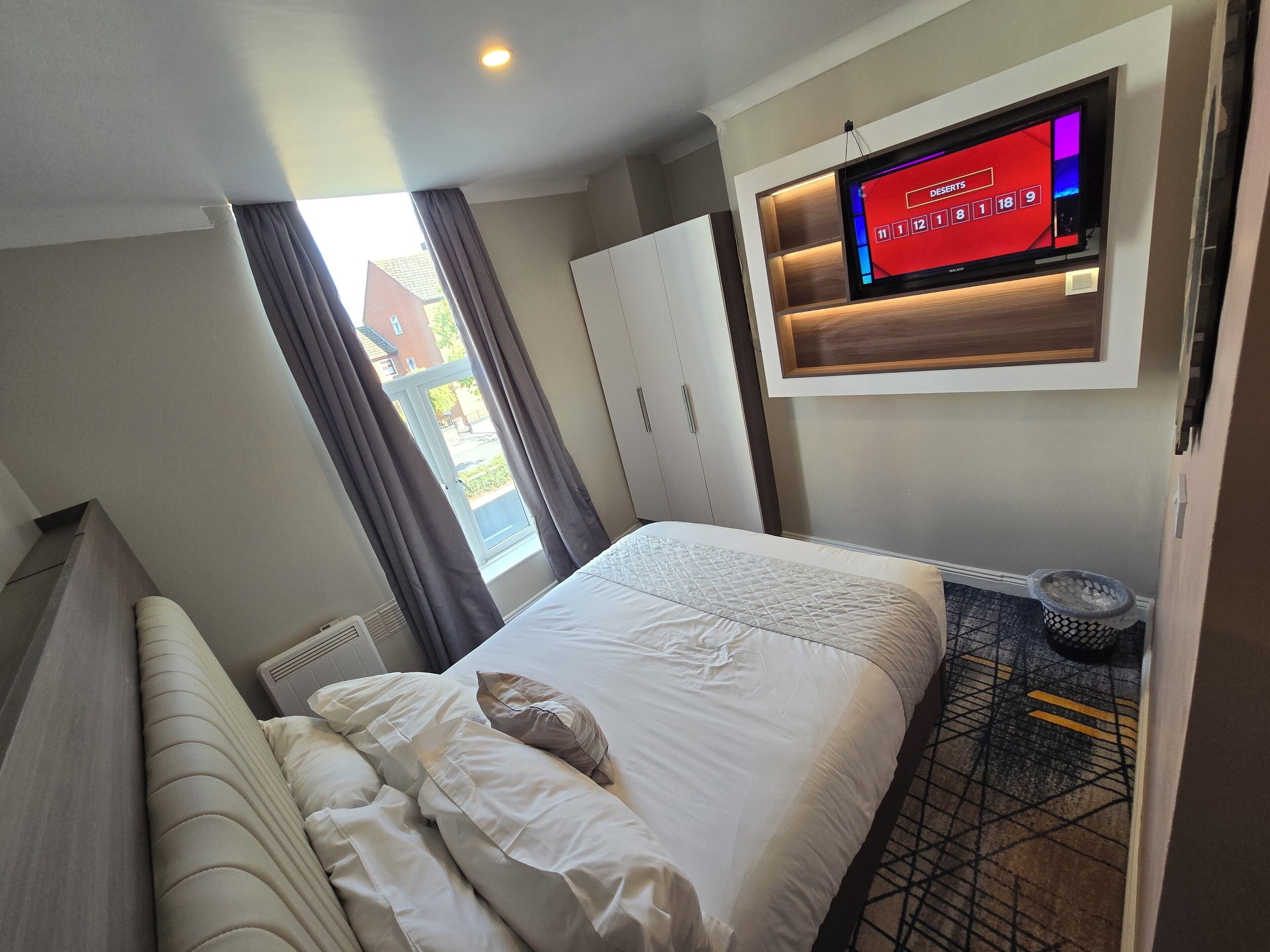 Habitación de hotel con cama, televisor montado en la pared, ventana con cortinas y radiador.
