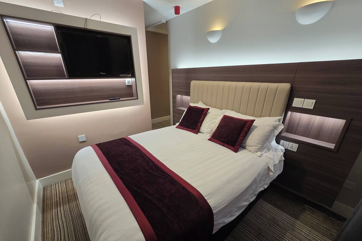 A hotel room with a large bed, a flat-screen TV mounted on the wall, and a modern headboard.
