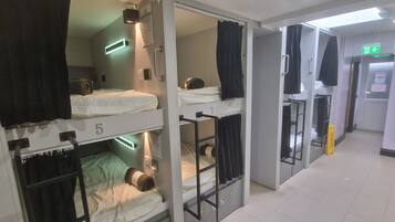 A hotel room with bunk beds, a bathroom with a shower, and a hallway with an exit sign.