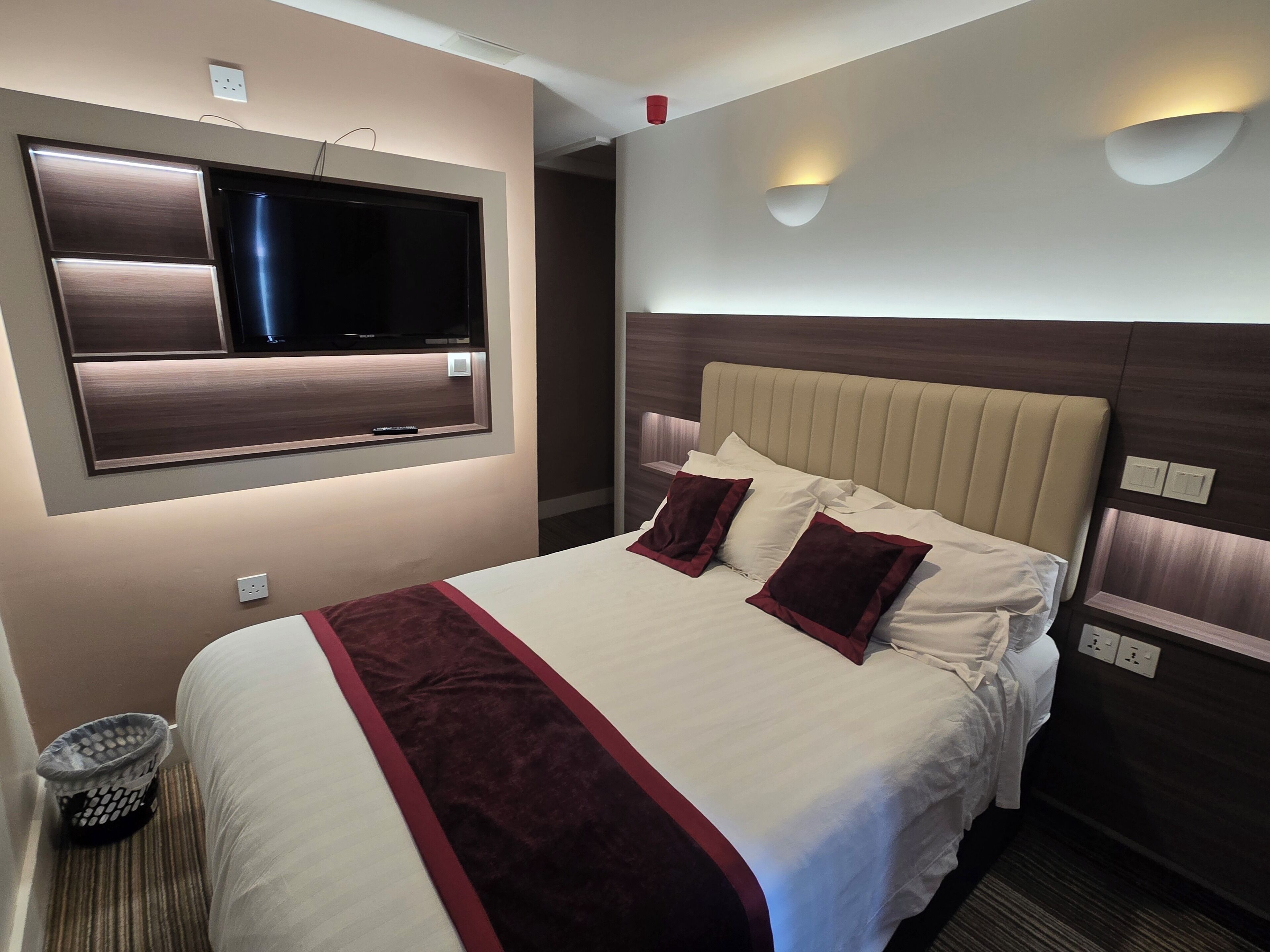 A hotel room with a large bed, a television mounted on the wall, and a wall-mounted light fixture.