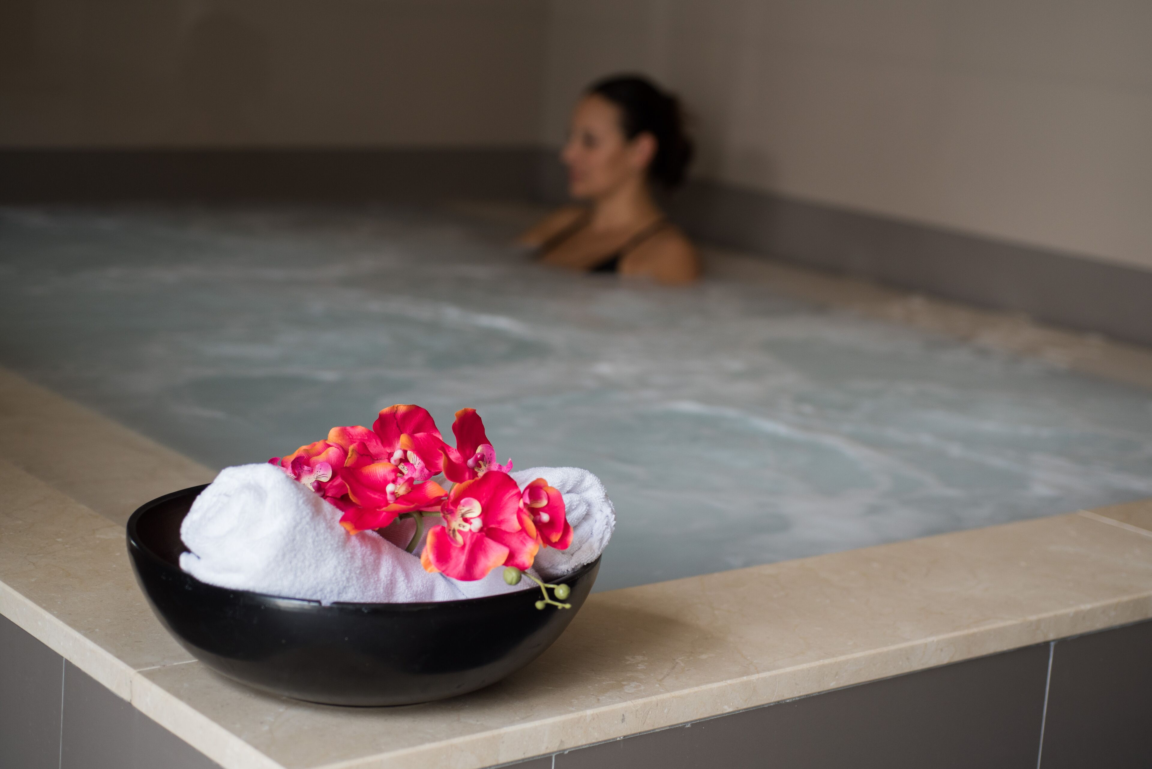 A spa setting with a black bowl containing a white towel and pink flowers on a counter.
