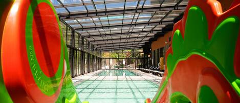A covered swimming pool with a glass ceiling, surrounded by colorful play structures.