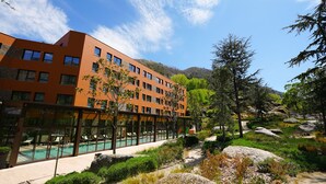 A modern hotel with a swimming pool, outdoor seating, and a mountainous backdrop. - Vila Galé Collection Serra da Estrela Hotel (Manteigas)