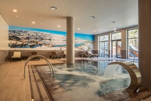Une piscine intérieure moderne agrémentée d’une cascade, de chaises longues et d’une fresque représentant un paysage enneigé.
