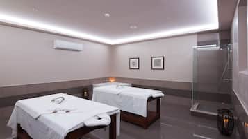 A spa room with two massage tables, a glass shower enclosure, and a wall-mounted air conditioner.
