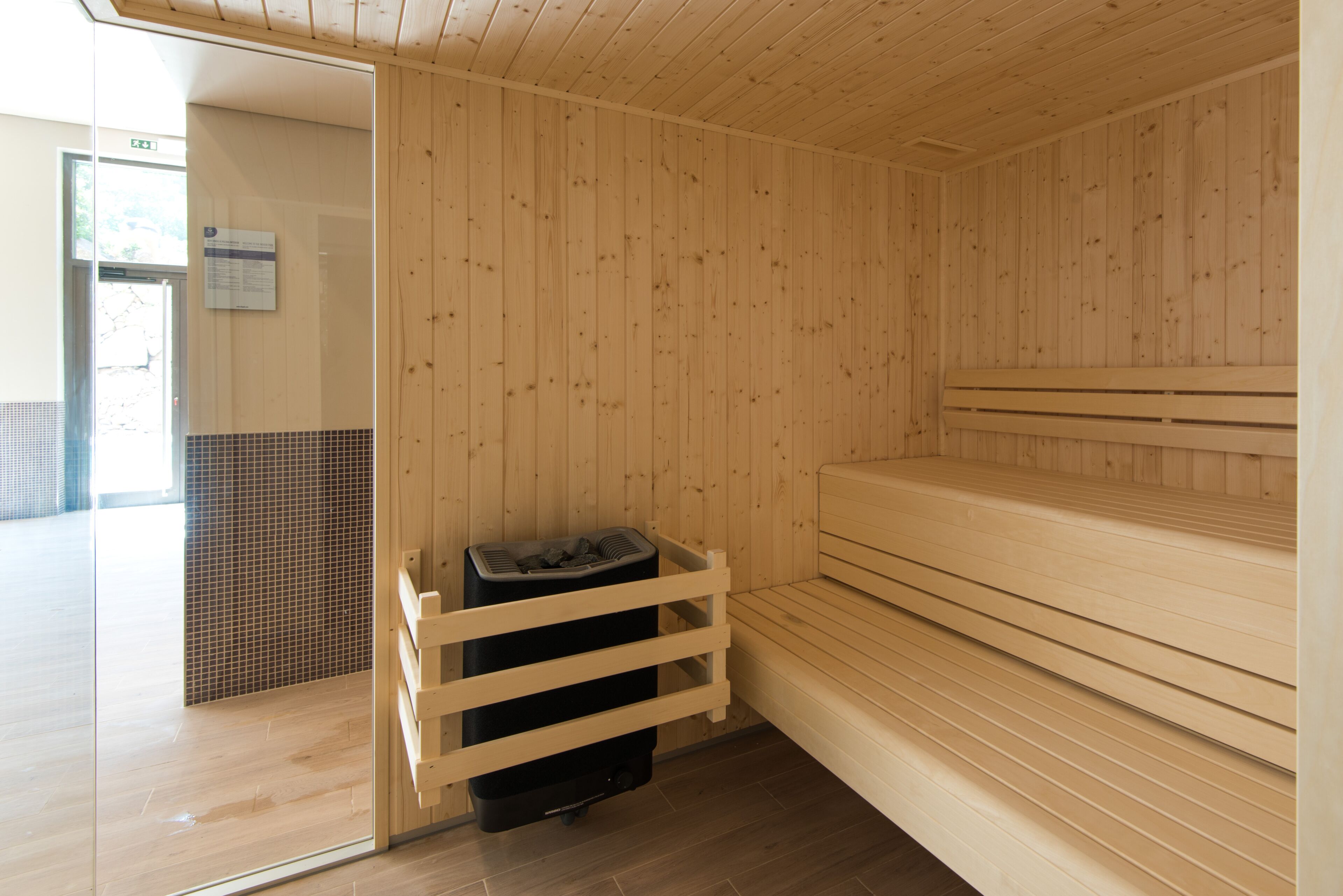 A sauna room with wooden walls and benches, a tiled floor, and a trash bin.