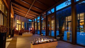 A modern interior with a fire feature, large windows, and a wooden ceiling. - Vila Galé Collection Serra da Estrela Hotel (Manteigas)