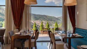 A restaurant with a table set for dining, a sofa, and a view of the landscape. - Vila Galé Collection Serra da Estrela Hotel (Manteigas)