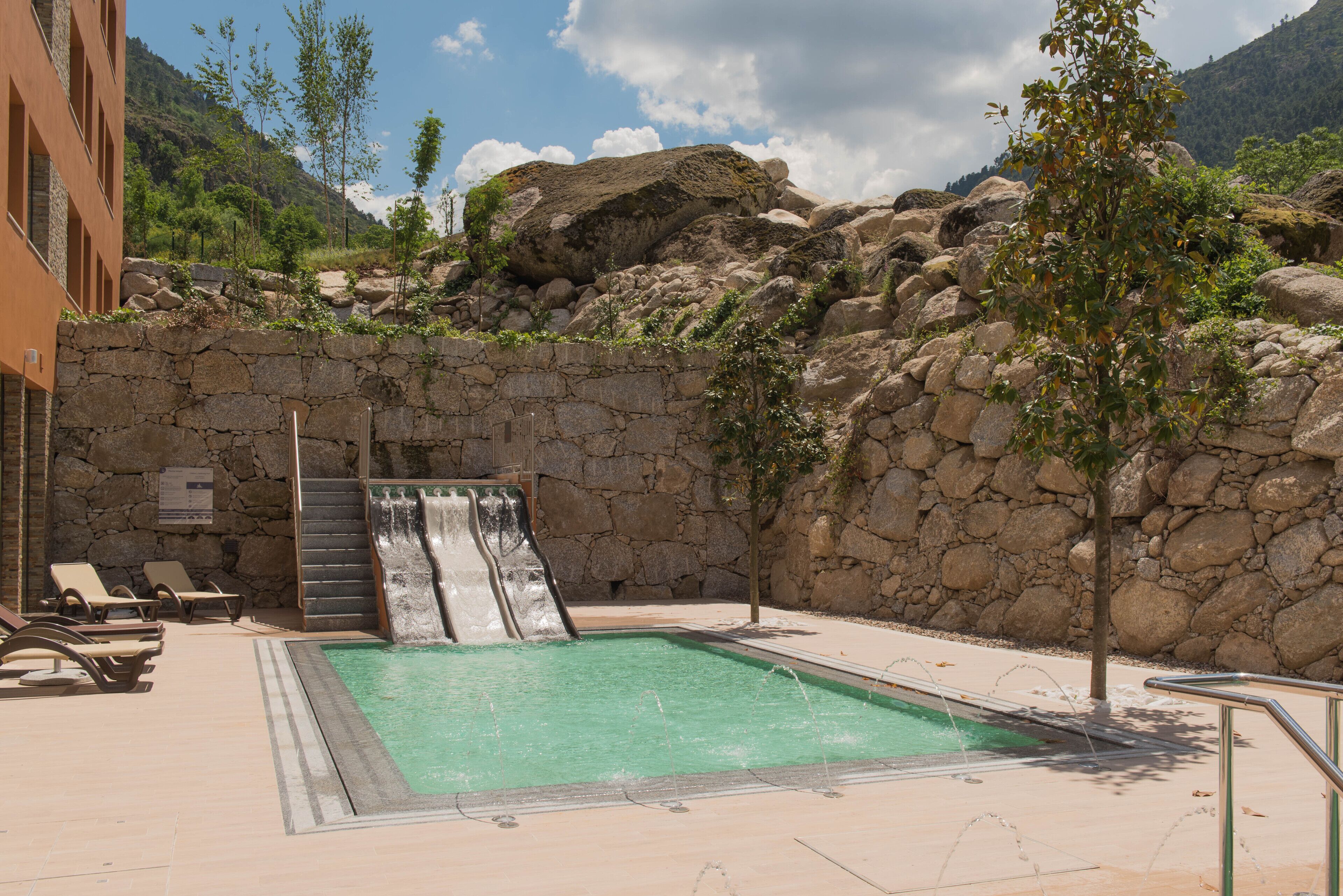 A pool area with a waterfall, lounge chairs, and a stone wall.