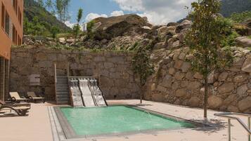 A pool area with a waterfall, lounge chairs, and a stone wall.