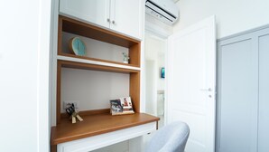 Een moderne kamer met een wit bureau, een grijze stoel, een houten plank met boeken en een klok, en een witte deur.