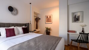 A neatly arranged bedroom with a large bed, a bedside table, a chair, a potted plant, and a framed picture on the wall. - Acropolis Grand Apartment (Athens)