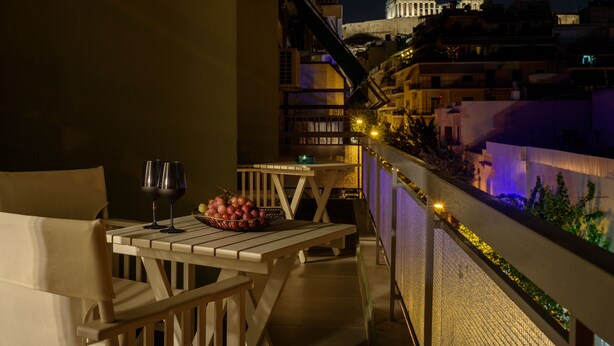 A balcony with a table, two chairs, a bowl of grapes, and two wine glasses. - Acropolis Grand Apartment (Athens)