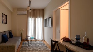 A living room with a sofa, a small table, a TV, and a dining area with a chair and a tray with a bottle and glasses. - Acropolis Grand Apartment (Athens)