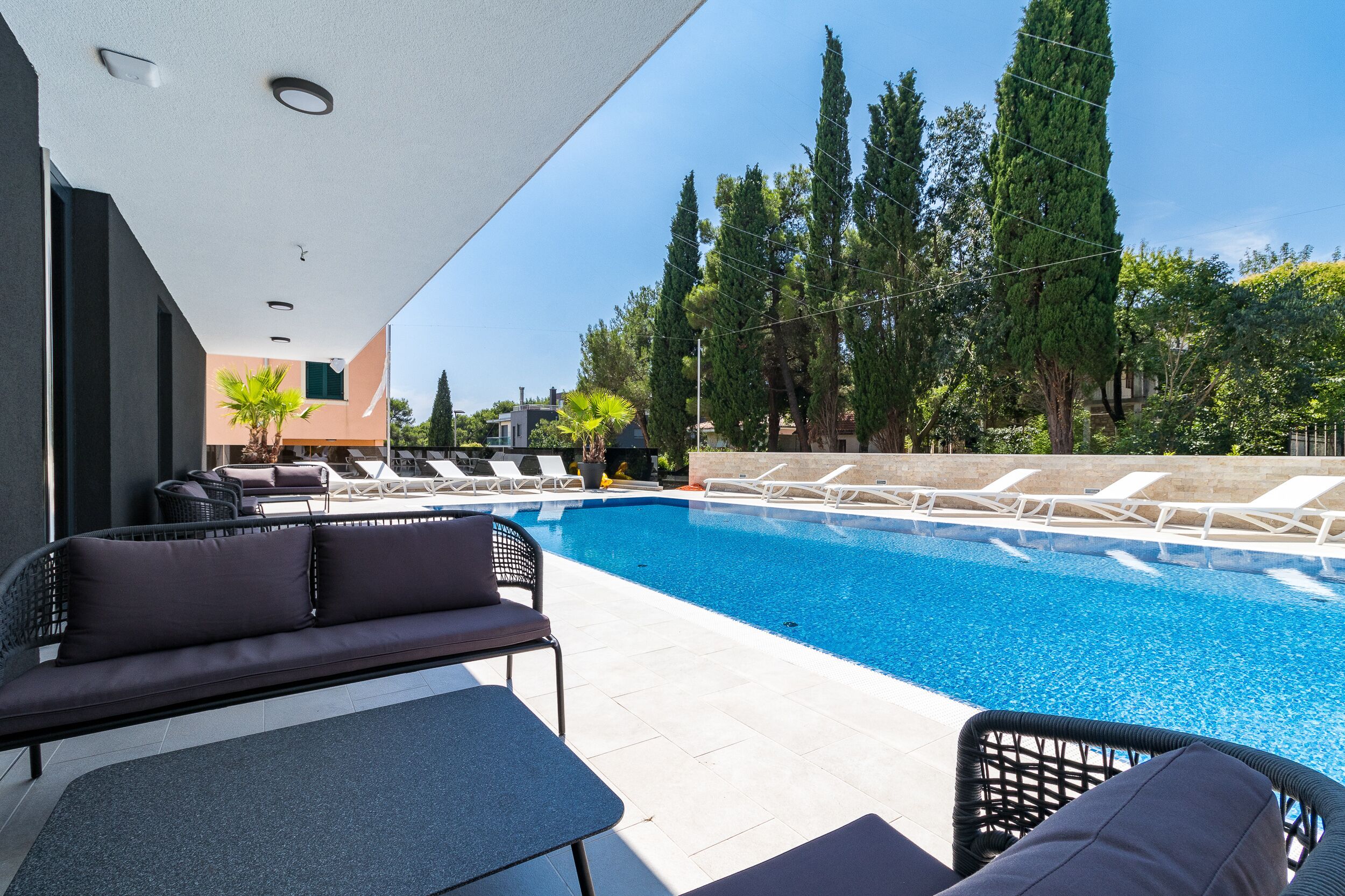 Un área de piscina moderna al aire libre con sillones de descanso y una zona de estar.